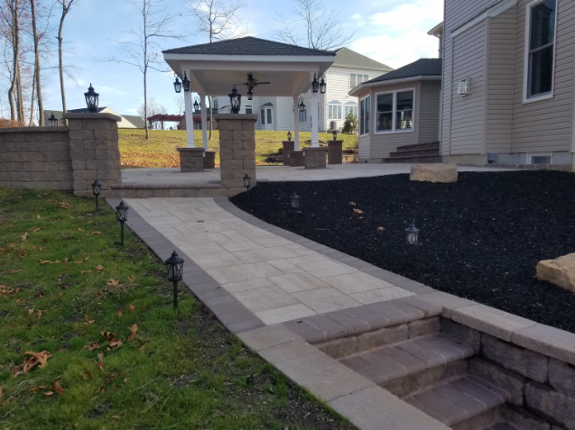 Patio with a stone walkway, steps, and gazebo in a backyard with landscaping.