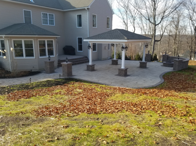 Backyard patio with gazebo, surrounded by brick walls and landscaping, with a large house in the background.