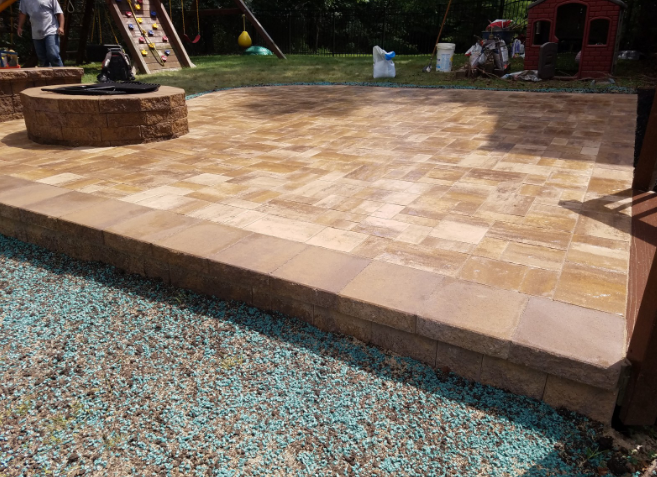 Stone patio with a low retaining wall, fire pit, and playground in the background.