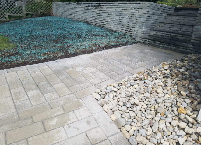 Paver patio leads to a stone wall and gravel area; newly seeded lawn in background.