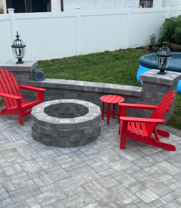 Backyard patio with fire pit, red Adirondack chairs, small red side table, and white fence.