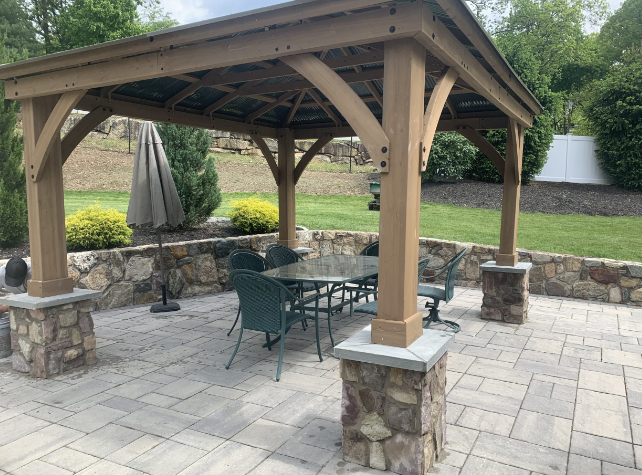 Gazebo with stone pillars, a dining table and chairs, and a paved patio.