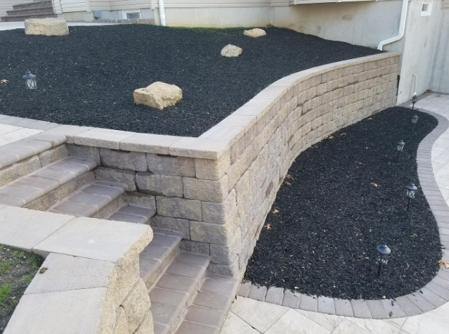 Stone retaining wall with steps, black mulch, and landscaping.