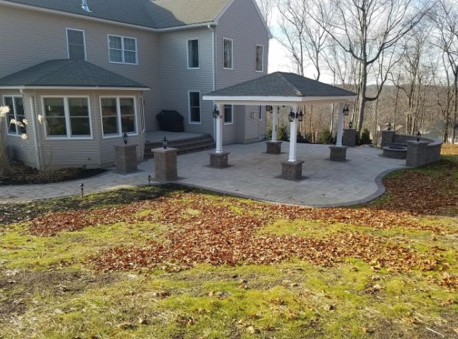 Backyard patio with a gazebo, seating area, and house. Concrete pavers, pillars, and fall leaves.