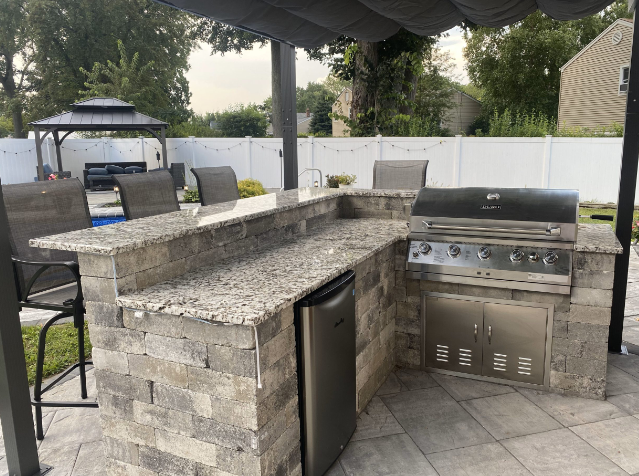 Outdoor kitchen with granite countertop, built-in grill, and bar seating.