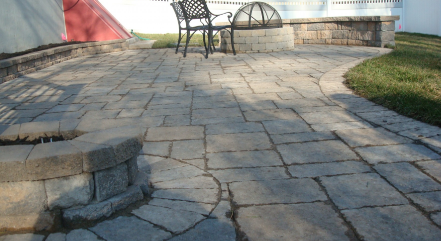 Stone patio with a fire pit, black chairs, and a curved edge leading to grass.