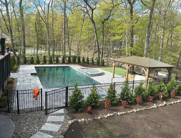 Pool area with pool, hot tub, gazebo, trees, and fence.