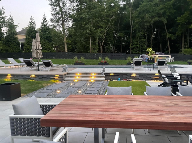 Outdoor pool area with a wooden table, chairs, and lounge chairs.