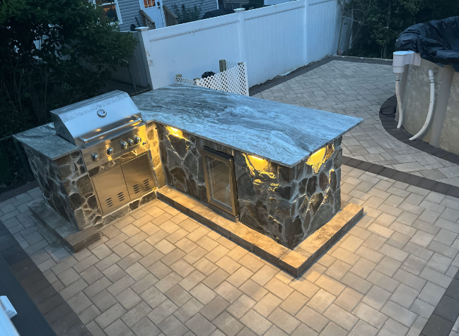 Outdoor kitchen with stone facade, granite countertop, stainless steel grill, and patio.