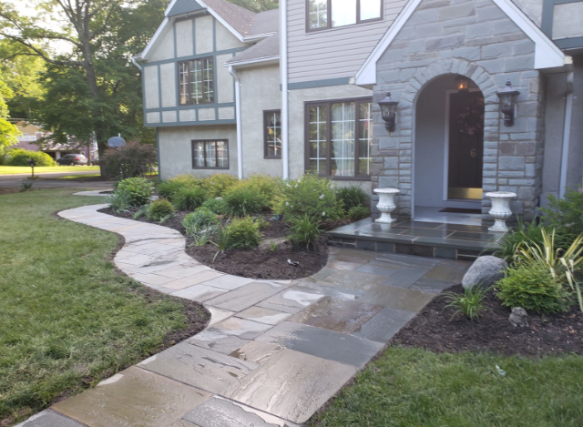 Stone pathway leading to a house with a stone archway entrance and landscaped beds.