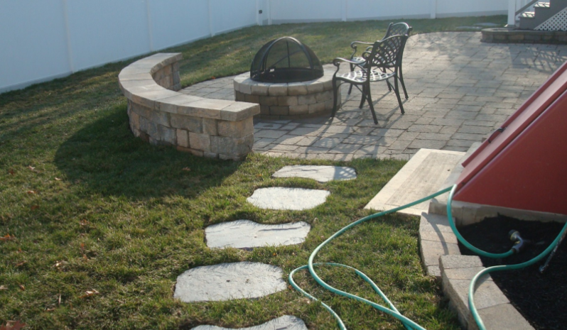 Stone fire pit and seating area with curved wall and stepping stones.