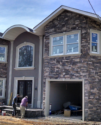 New house under construction, stone facade, stucco, arched window, two men working near the entrance, garage open.