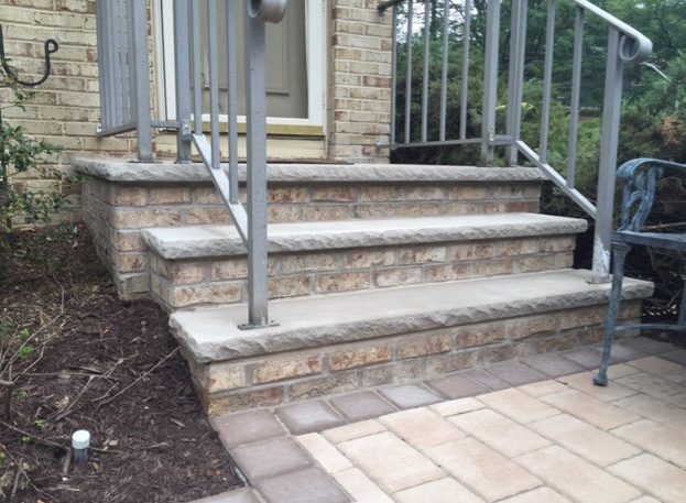 Brick steps with gray concrete accents and metal railings lead to a doorway.