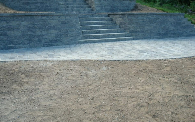 Stone steps leading up to a wall, paved area in front, dirt ground.