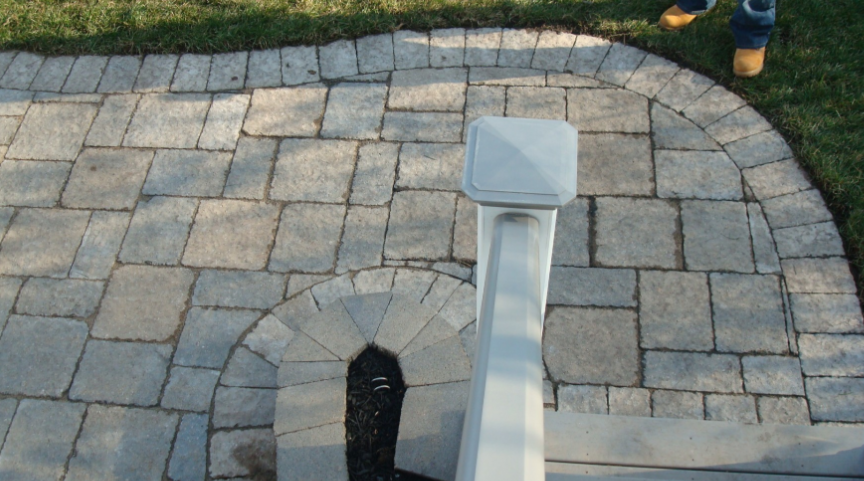 Brick patio with curved border, white railing, and person's legs.