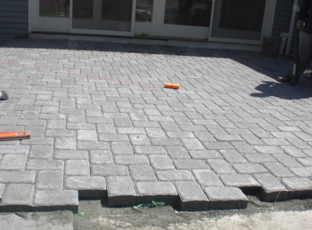 Patio pavers being installed, gray bricks in a herringbone pattern near sliding doors.