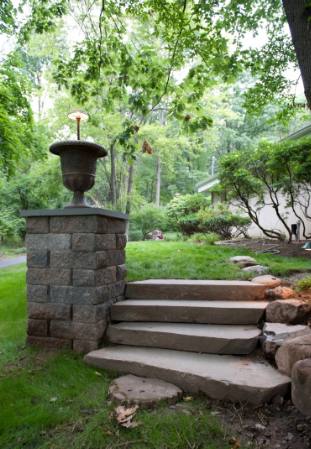 Stone steps and pillar with urn-shaped light fixture in a wooded yard.