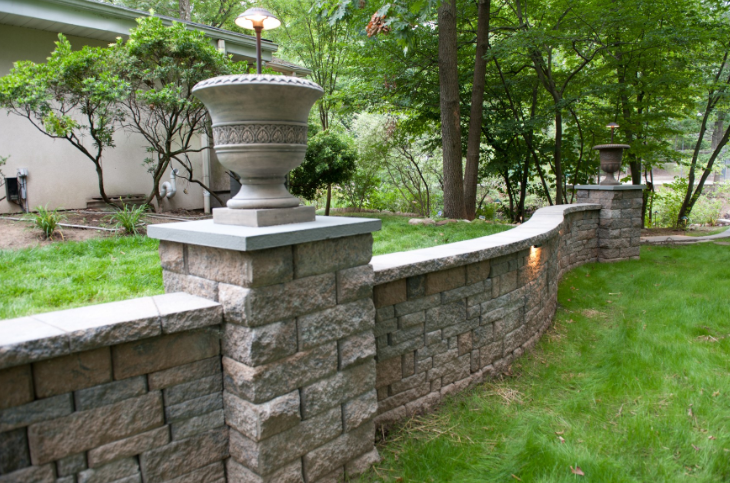 Stone retaining wall with decorative urns, lights, and green grass.