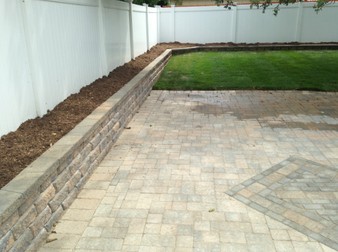 Stone patio with retaining wall, lawn, and white fence.