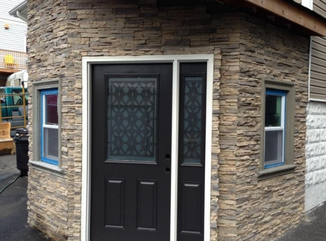 Exterior of a building with a stone facade, black door, and two white-framed windows; blue tape around windows.