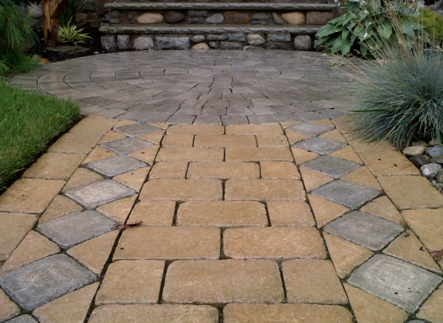 Stone walkway leading to steps and a garden. The walkway has a brick and diamond pattern.