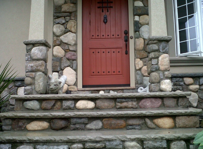 Stone steps and pillars frame a red wooden door.