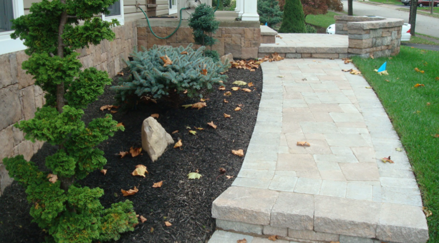Stone walkway leading to a house with landscaping, including a bonsai tree and mulch.