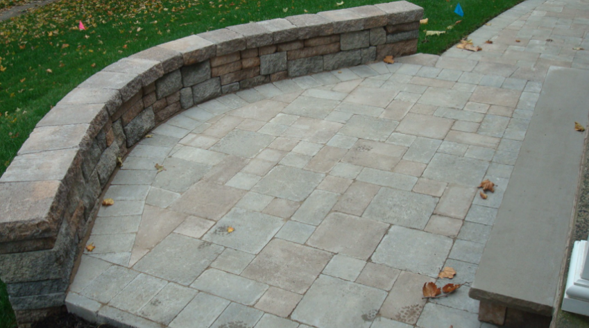 Curved stone retaining wall on a paved patio with steps leading to a lawn.
