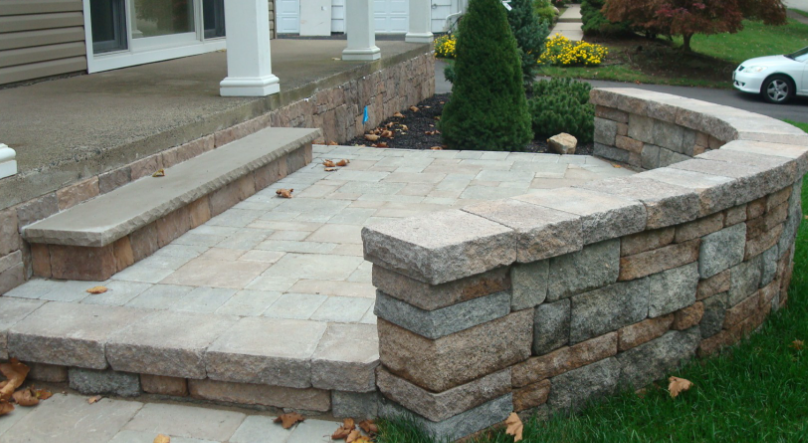 Stone patio with built-in bench and curved retaining wall, leading to a home entrance.