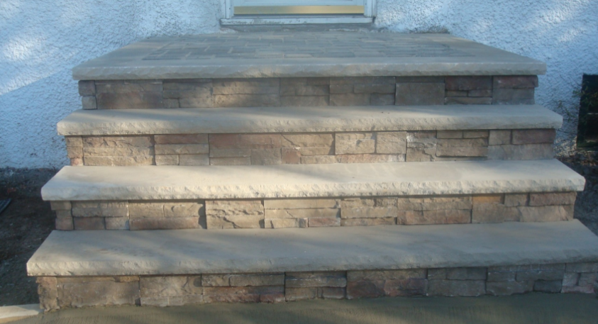 Stone steps leading up to a door. Three steps with a concrete top, stone facade.