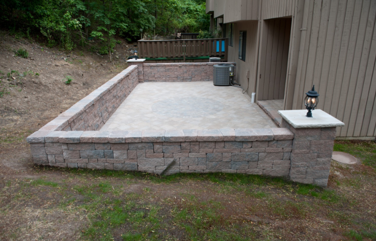 Stone-walled patio beside a building with a light fixture on a pillar. Grass in the foreground.