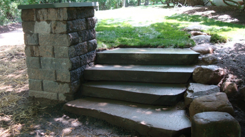 Stone steps leading up to a grassy area, with a stone retaining wall on the left.