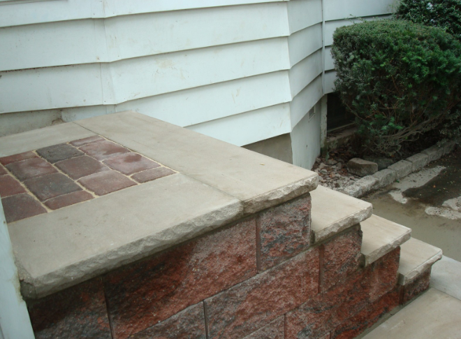 Brick and stone steps leading up to a building entrance with white siding and a small bush.