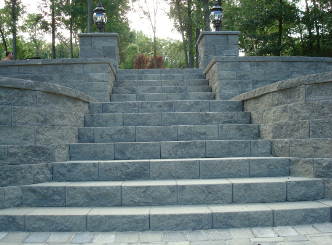 Stone steps leading upwards, flanked by low walls with lamps, set in a natural outdoor environment.