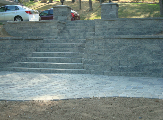 Stone steps lead up a retaining wall with cars parked nearby.