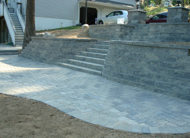 Stone paved patio with stairs and retaining walls leading up to a house and garage.