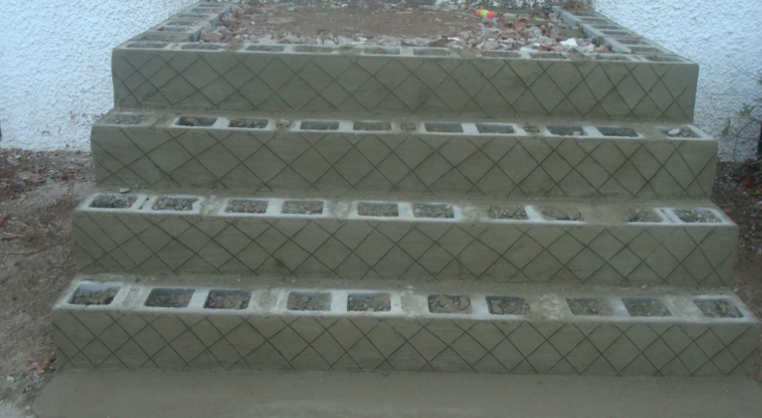 Concrete block steps, four risers, with a crisscross pattern on the sides, leading up to an unfinished area.