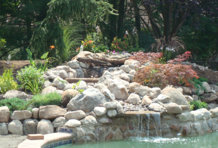 Waterfall cascading into a pool, surrounded by rocks, lush greenery, and flowers.