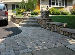 Stone paver driveway leading to steps and a house with a car parked on the left.