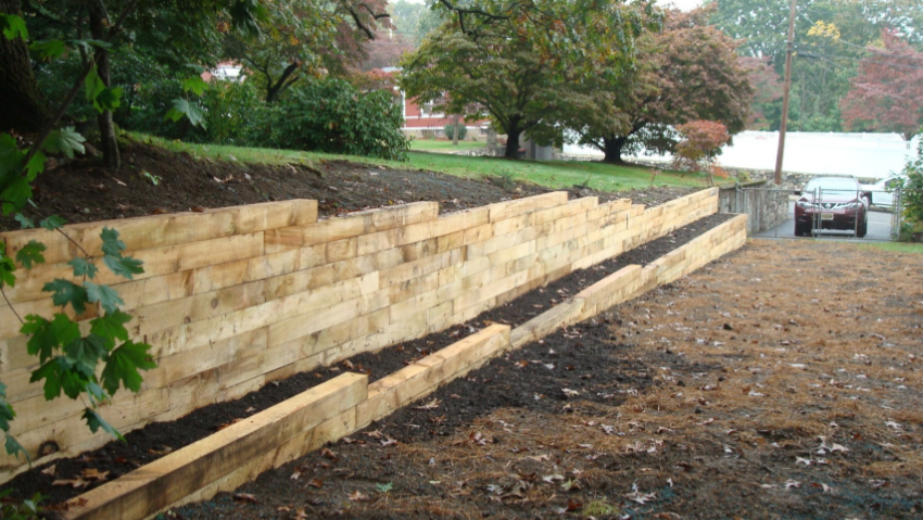 Wooden retaining wall built along a sloped driveway, car parked at the top.