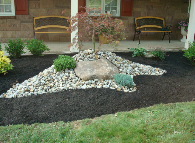 Landscaped front yard with a rock and stone garden bed and small tree.