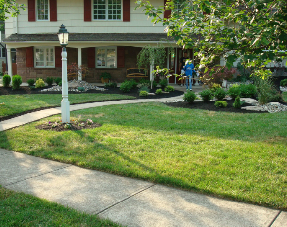 Lawn with walkway leading to a house with a porch. Landscaping and a lamp post are in the yard.
