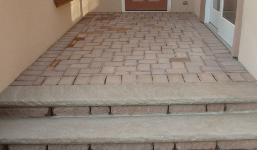 Brick patio and steps leading to a doorway; beige walls, brown brick, concrete steps.