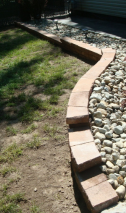 Brick edging along a curved stone bed, separating it from grass.