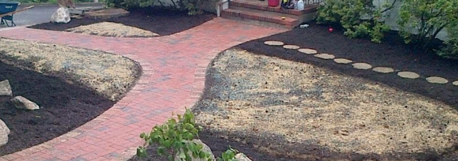 Brick pathway with mulch and stepping stones in a landscaped yard.