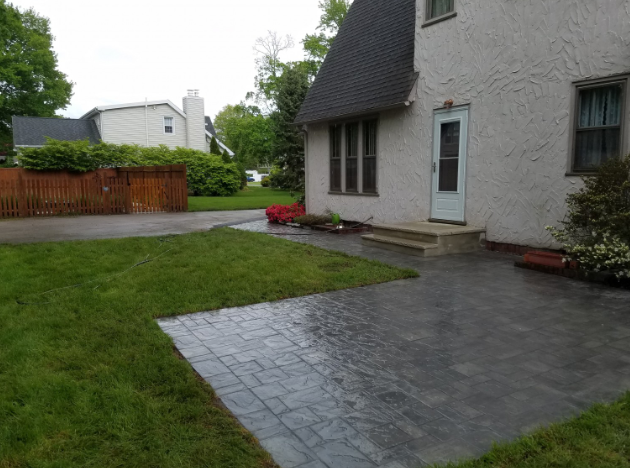 Backyard with paved patio, grass lawn, and house with a door and windows.