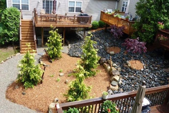 Backyard deck with trees, landscaping and pebble stone ground cover.