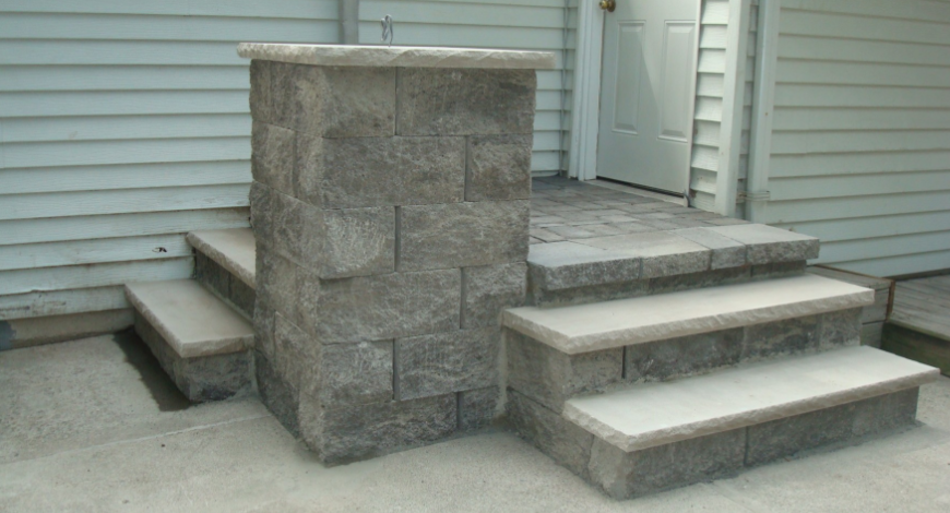 Stone steps and pillar leading to a white door, set against light blue siding.