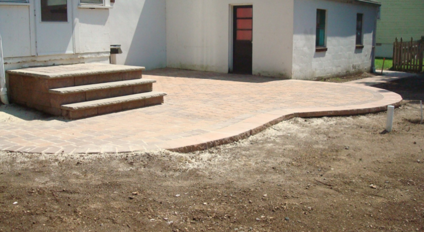 Brick patio with curved edge and steps leading to a white building.