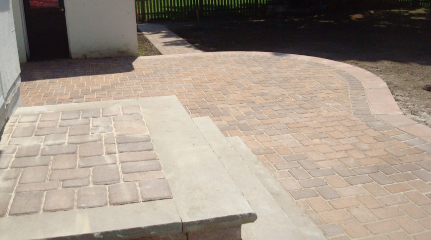 Brick paver patio and steps leading to a door, with a curved border and a grassy area in the background.